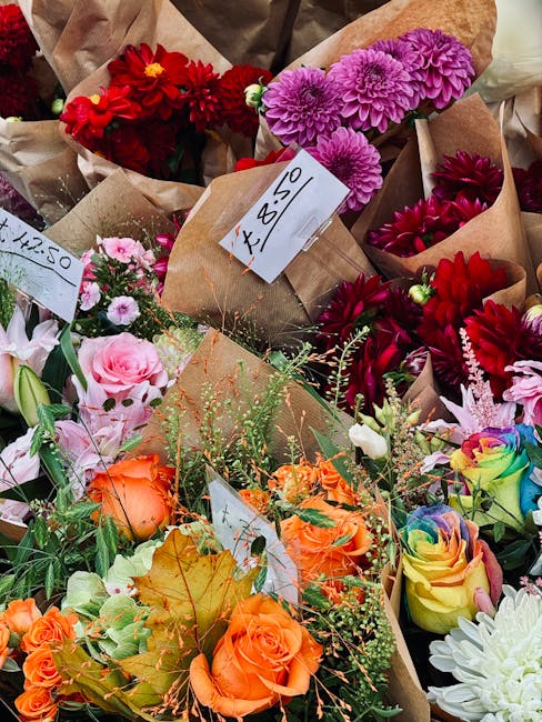 An assortment of floral bouquets featuring vibrant and pastel-colored flowers arranged in brown craft paper wrapping. The bouquet at the forefront includes orange roses, surrounded by green foliage an